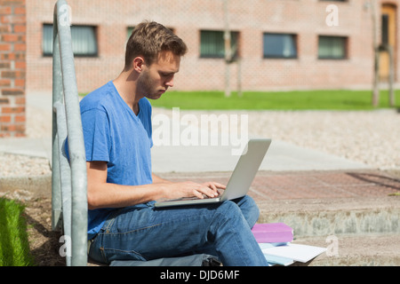 Frowning handsome student sitting on stairs using laptop Stock Photo