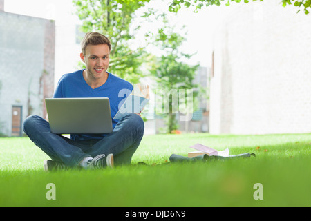 Smiling handsome student sitting under tree studying Stock Photo
