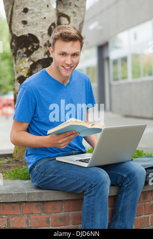Smiling handsome student sitting on wall studying Stock Photo