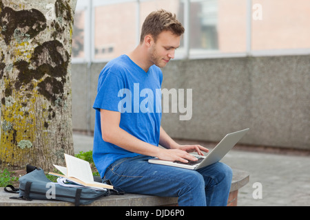 Focused handsome student sitting on wall studying Stock Photo