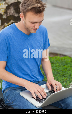 Peaceful handsome student sitting on wall studying Stock Photo