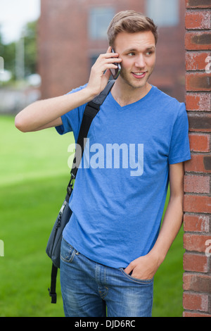 Happy handsome student leaning against wall phoning Stock Photo