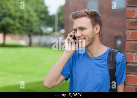 Smiling handsome student leaning against wall phoning Stock Photo
