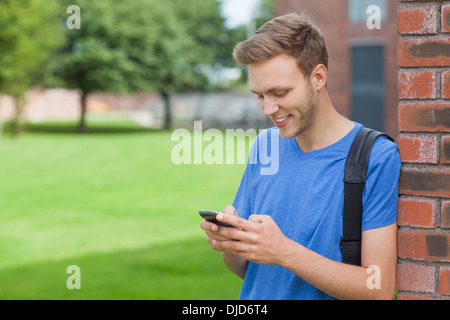 Smiling handsome student leaning against wall texting Stock Photo