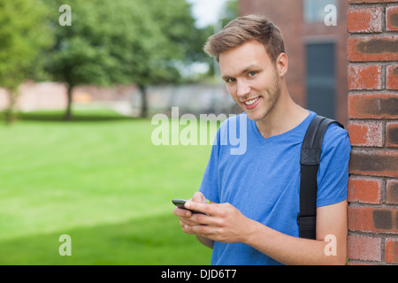 Cheerful handsome student leaning against wall texting Stock Photo