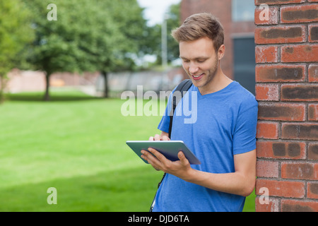 Smiling handsome student leaning against wall using tablet Stock Photo