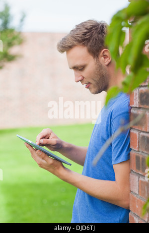 Happy handsome student leaning against wall using tablet Stock Photo