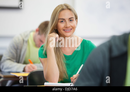 Pretty blonde student taking notes in class smiling at camera Stock Photo