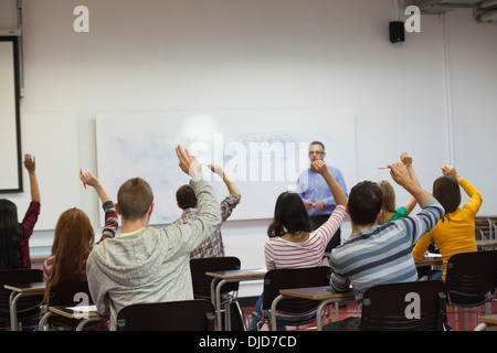 Students listening to their teacher in classroom and raising their hands Stock Photo