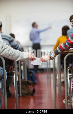 Students passing notes to each other in classroom behind teachers back Stock Photo