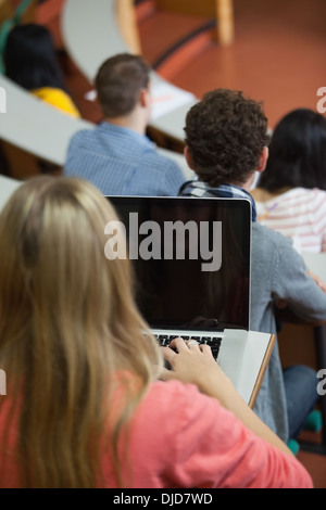 Blonde student sitting in a lecture using her laptop Stock Photo