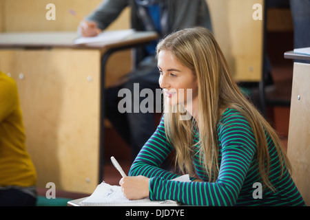 Smiling blonde student taking notes in a lecture hall Stock Photo