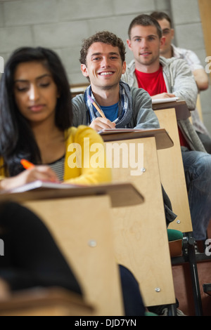 Smiling handsome student taking notes in a lecture hall Stock Photo