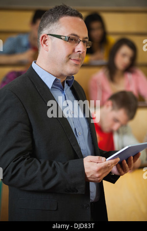 Lecturer holding tablet pc in front of class in lecture hall Stock Photo