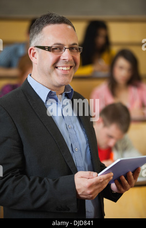 Lecturer holding tablet pc in front of class in lecture hall smiling at camera Stock Photo