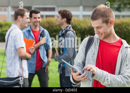 Cheerful male student using his tablet in front of his classmates outside Stock Photo