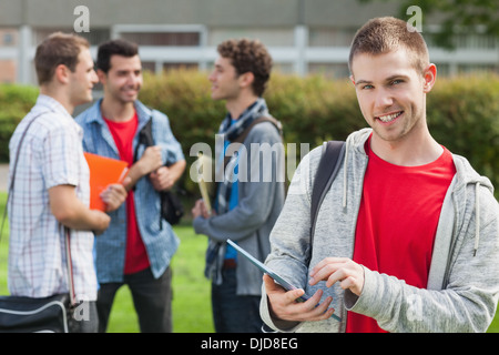 Happy male student using his tablet in front of his classmates outside Stock Photo