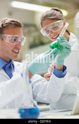 Two happy students looking at green liquid and taking notes Stock Photo