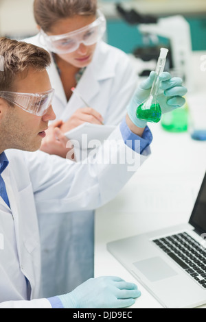 Two students examining green liquid and taking notes Stock Photo