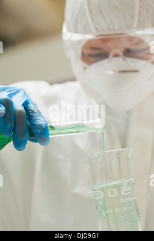 Lab assistant with mask pouring liquid in beaker Stock Photo