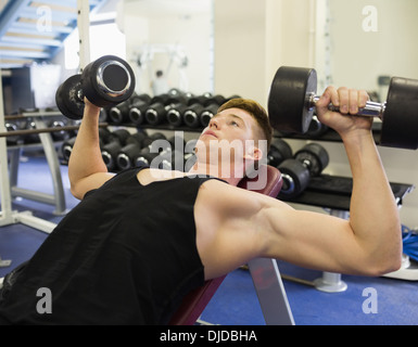 Muscular focused man lying on bench training with dumbbells Stock Photo