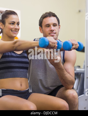 Instructor assisting smiling woman lifting dumbbells Stock Photo