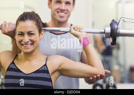 Instructor helping smiling woman lifting barbell Stock Photo