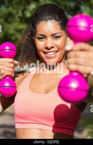 Smiling fit woman exercising with dumbbells in park Stock Photo