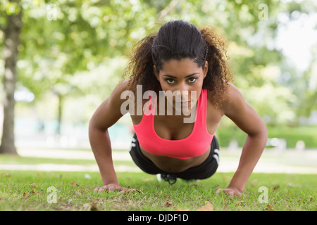 Beautiful serious young woman doing push ups in park Stock Photo