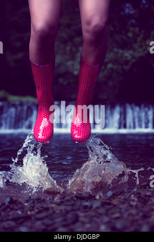 Woman in red gumboots jumping in water Stock Photo