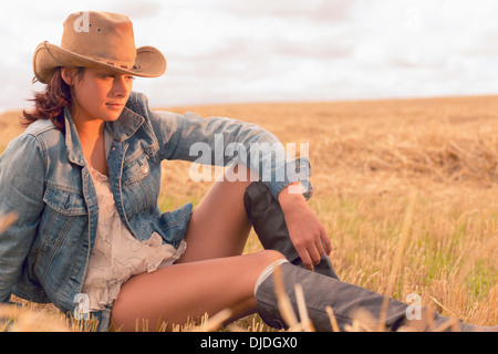 Beautiful young woman in hat sitting at cereal field Stock Photo