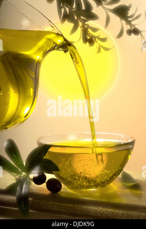 Olive oil being poured from a jug into a glass bowl Stock Photo