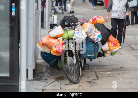 Bicycle on a pavement in the West End of London with possessions of a homeless vagrant in plastic carrier bags Stock Photo
