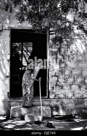 Old Indian woman coming out of Sri Sathya Sai Baba mobile outreach hospital clinic. Andhra Pradesh, India. Monochrome Stock Photo