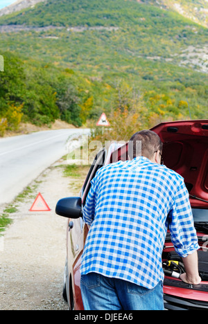 Adult man is standing near his broken car waiting for tow Stock Photo