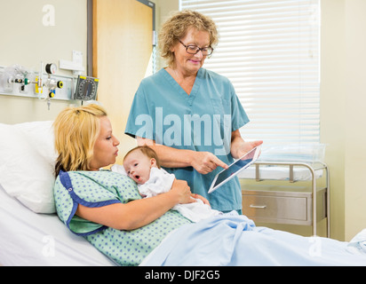 Nurse Explaining Reports On Digital Tablet To Woman With Babygir Stock Photo