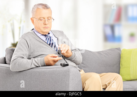 Mature diabetic patient on sofa measuring sugar level in blood using glucometer at home Stock Photo
