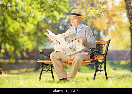 Senior man sitting on a bench and reading a newspaper in autumn Stock Photo