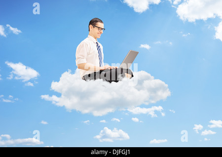 Young businessman on clouds working on a laptop Stock Photo