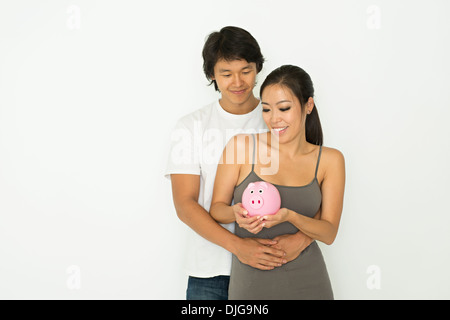 A young Asian couple hug, smiling and holding a piggy bank, money and saving concept. Stock Photo