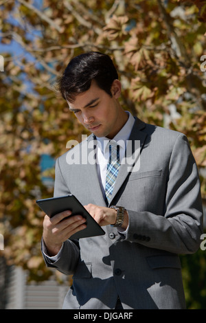 A young business man looking down, browsing and reading his ipad, tablet. He wears a gray business suit. Stock Photo