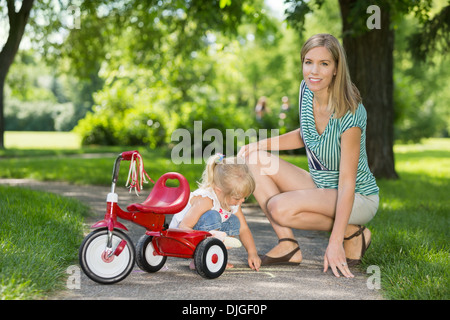 Mother With Daughter Crouching By Tricycle On Walkway Stock Photo