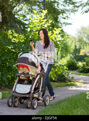 Woman With Baby Carriage Using Cell Phone In Park Stock Photo