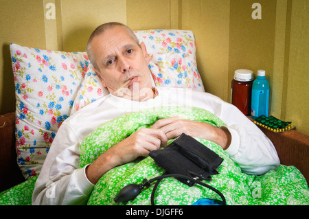 Sick man lying in bed and measuring the temperature with a thermometer Stock Photo