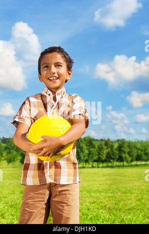 Beautiful happy smiling Asian boy holding yellow volleyball standing in the park Stock Photo