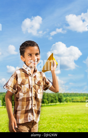 Cute little 6 years old boy holding blue paper airplane on bright sunny day Stock Photo