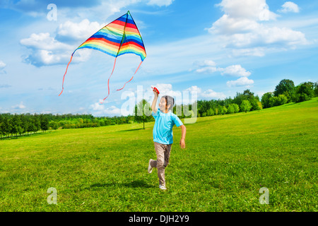 Little boy in blue shirt running with kite in the field on summer day in the park Stock Photo