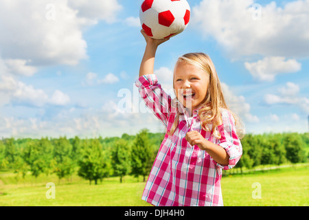 Cute little blond girl in pink shirt throwing soccer ball laughing Stock Photo