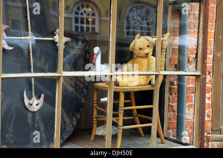 Teddy bear sitting on a chair in the window of an antique shop in Arundel, West Sussex, England UK Stock Photo