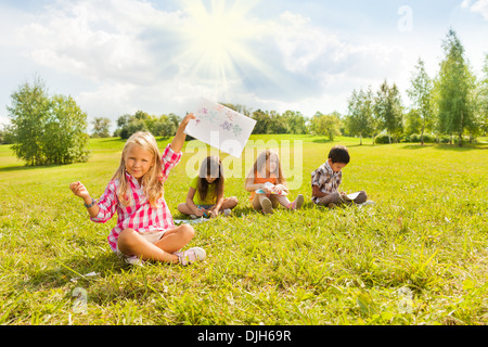 Little blond girl showing off her painting with her friends drawing on background Stock Photo